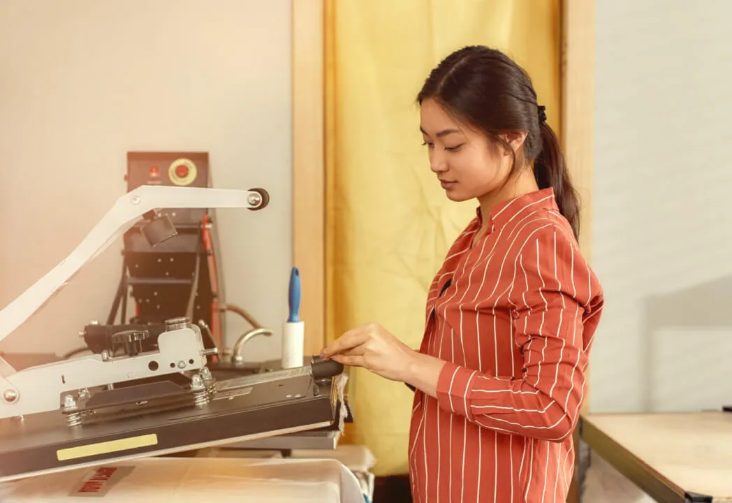 A young woman is using a screen printer to make a custom shirt
