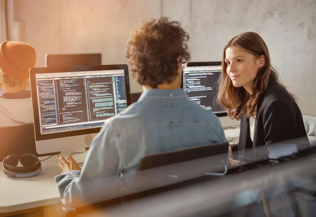 Two telecom business employees speak while seated at a desk