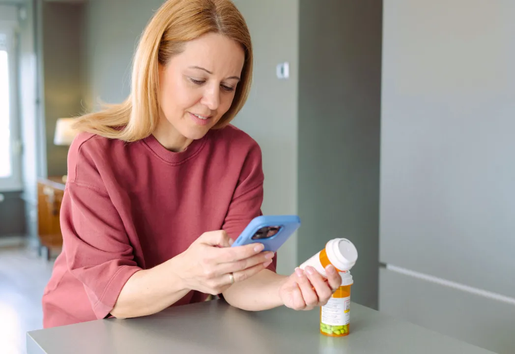 A woman holds a tablet in one hand while looking at her phone with a focused expression.