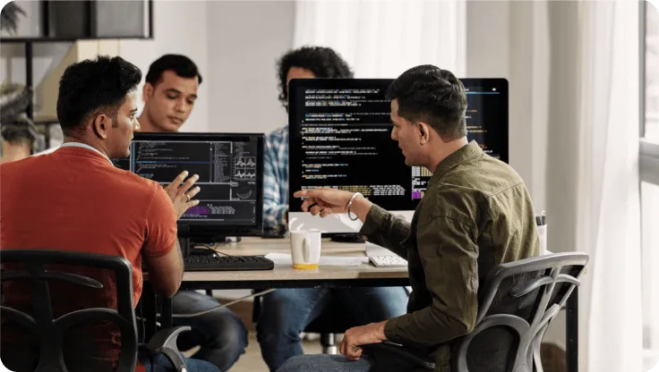 Two IT colleagues discussing a process in front of their desktop screens
