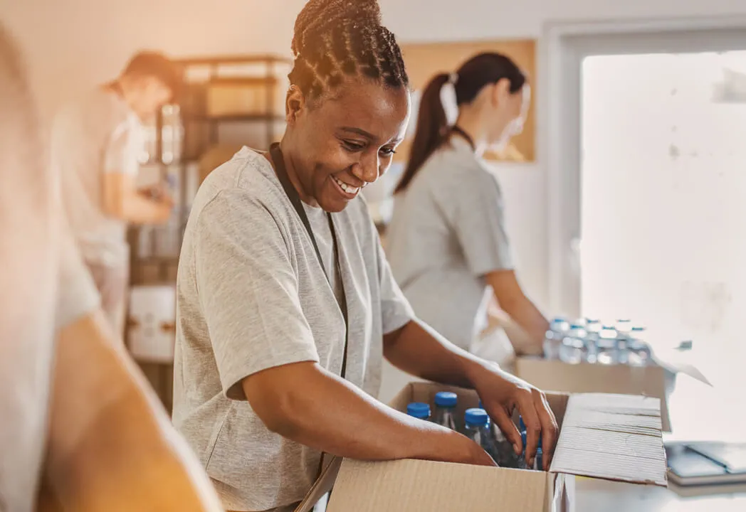 A smiling volunteer packs a box of water bottles